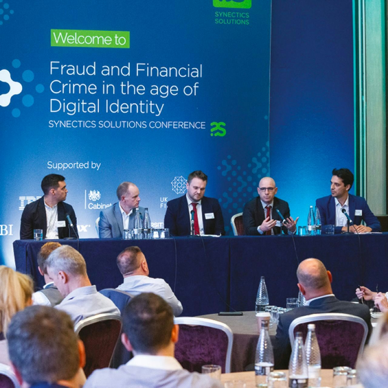 Panel discussion at the Synectics Solutions Conference on 'Fraud and Financial Crime in the age of Digital Identity,' featuring speakers at a table in front of an audience. 