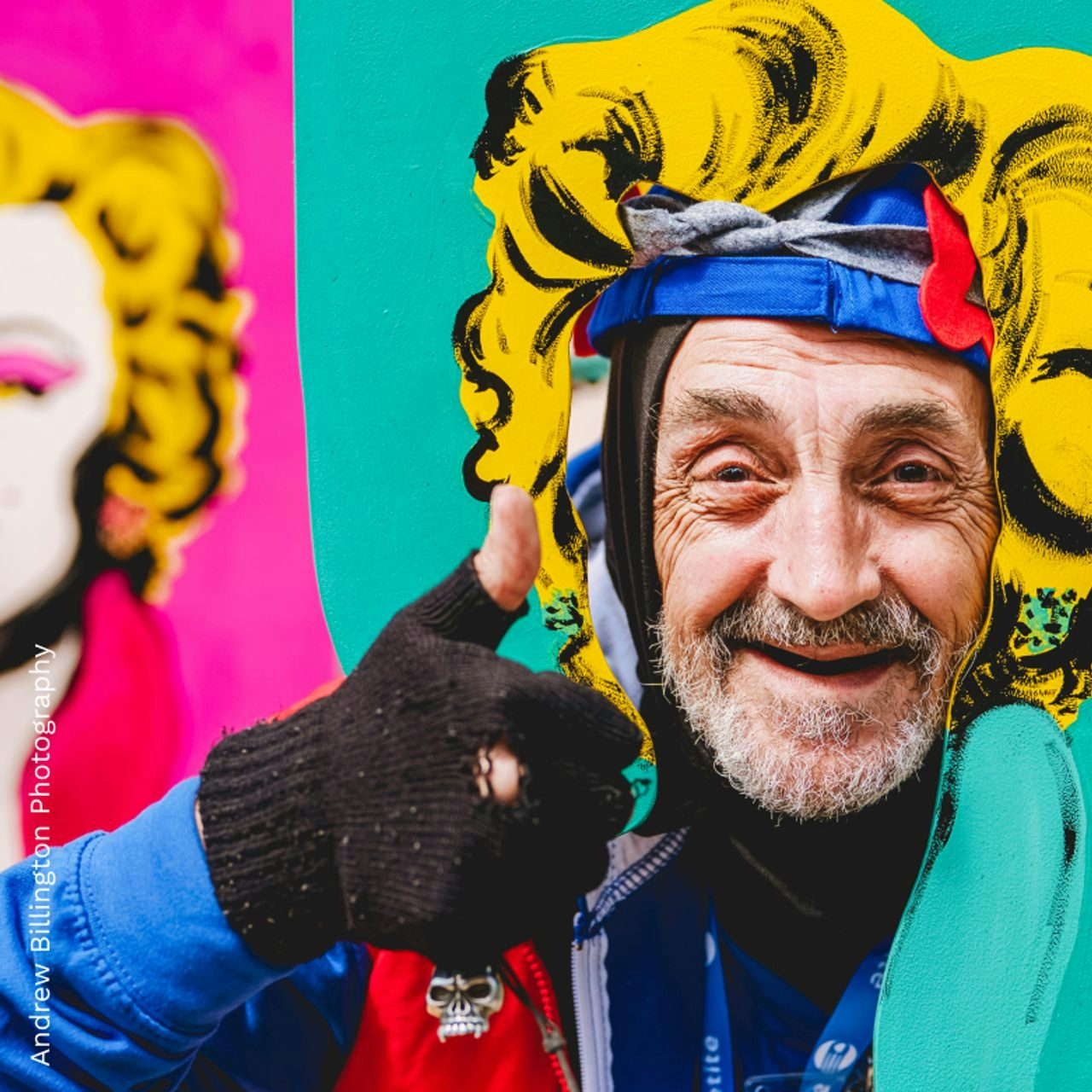Man smiling through cut out of a colourful display with a silhouette of a woman as the background. Photo credited to Andrew Billington Photography.
