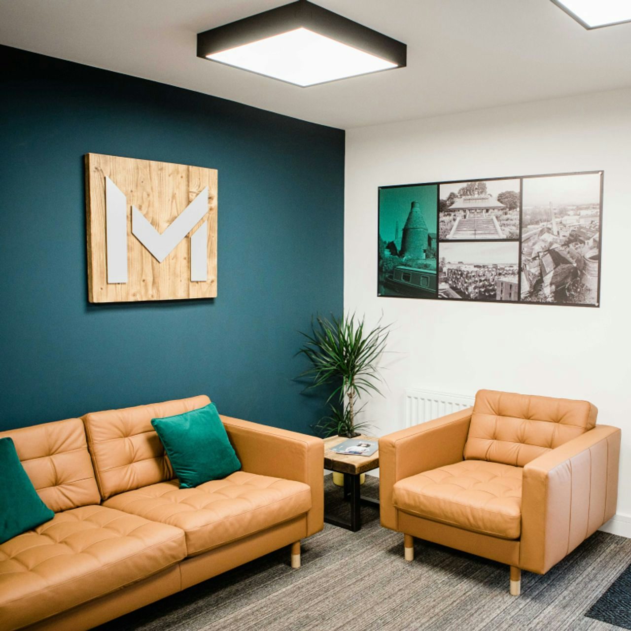 Office waiting area with teal accent wall featuring a company logo, leather seating, and urban-themed wall art, embodying a professional yet welcoming environment.